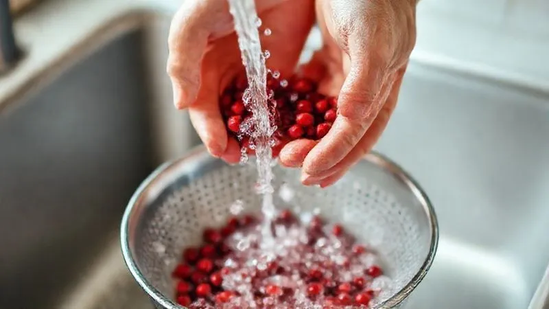 A person's hands gently rinsing red beans under cold running water in a colander, with a blurred background of a clean kitchen sink. The image conveys careful preparation and cleanliness. photorealistic, professional photography, 8K, cinematic lighting, sharp focus, depth of field, shot on a high-end DSLR.