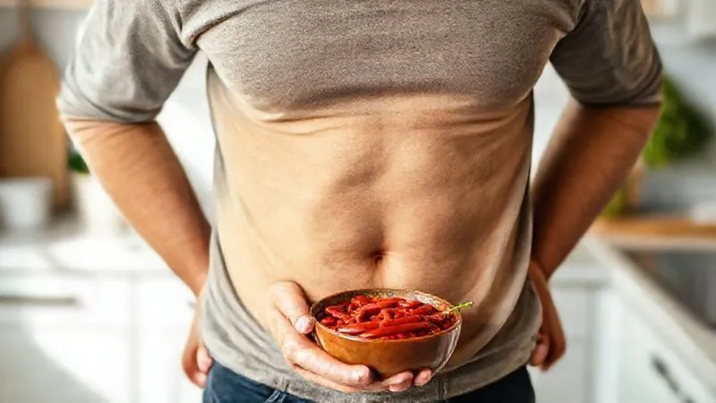 A person smiling confidently while holding a bowl of red bean chili, their stomach looking flat and comfortable, set against a bright, clean kitchen background. The image conveys health, happiness, and digestive comfort. photorealistic, professional photography, 8K, cinematic lighting, sharp focus, depth of field, shot on a high-end DSLR.