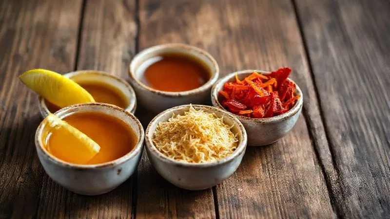 photorealistic, professional photography, 8K, cinematic lighting, sharp focus, depth of field shot of small ceramic bowls neatly arranged on a rustic wooden table, each containing a different flavor enhancer: bright yellow lemon wedges, a rich amber liquid of maple syrup, a pile of golden nutritional yeast flakes, and vibrant red sun-dried tomatoes. The composition is artfully lit, highlighting the textures and colors of the ingredients.