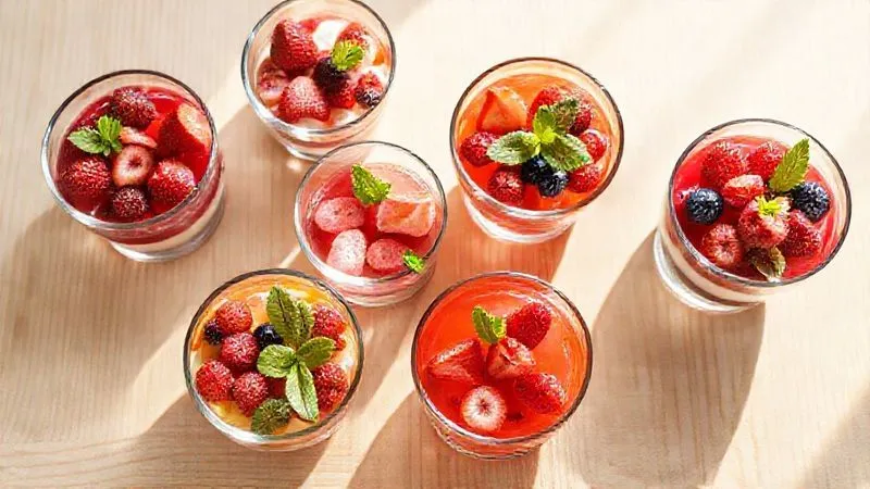 Photorealistic professional photography, top-down view of various glass bowls filled with colorful fruit jelly and protein layers, garnished with fresh berries and mint. The bowls are arranged neatly on a light wooden table, with natural daylight streaming in. Sharp focus on the desserts, with a clean background. 8K hyper-detailed, shot on a high-end DSLR.