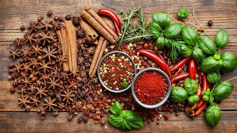 A vibrant, photorealistic flat lay of an array of fresh spices and herbs, including whole peppercorns, star anise, cinnamon sticks, dried chilies, fresh rosemary, thyme, basil, and a small bowl of colorful spice blend. The composition is artfully arranged on a rustic wooden table with cinematic lighting, sharp focus on the textures, 8K hyper-detailed, professional food photography.