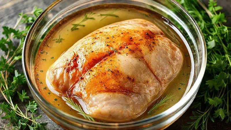 Photorealistic image of a turkey fillet marinating in a clear brine solution in a glass bowl, surrounded by fresh herbs, with dramatic lighting, sharp focus, 8K.