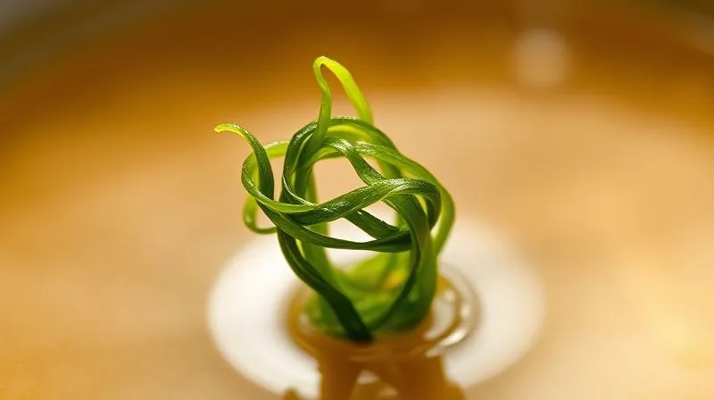 A photorealistic macro shot of a single, delicate strand of rehydrated wakame seaweed, beautifully unfurled and gently floating in a clear, subtly steaming dashi broth. The focus is incredibly sharp on the intricate texture and vibrant green color of the seaweed, with a soft, inviting bokeh background that suggests warmth and freshness. Shot on a high-end DSLR with a macro lens, 8K hyper-detailed.
