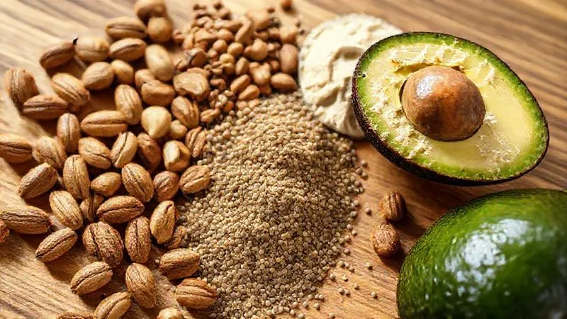 A close-up, photorealistic image of various healthy ingredients for a fit nut butter mousse spread on a wooden table: whole almonds, cashews, chia seeds, a scoop of protein powder, and a ripe avocado, all in natural, soft light. 8K, cinematic lighting, sharp focus, depth of field, shot on a high-end DSLR.