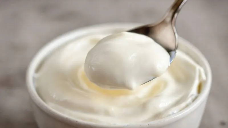 A close-up, photorealistic shot of homemade vegan yogurt, with a spoon gently scooping a creamy portion, showing its texture and inviting appearance. Soft, natural light, minimalist background.