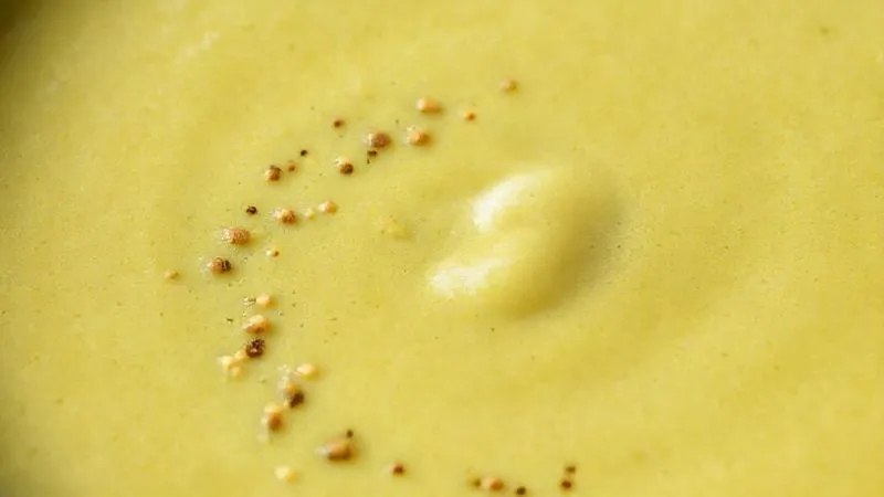Photorealistic close-up of a perfectly smooth, thick creamy celery soup, with tiny chia seeds barely visible on the surface, emphasizing a rich texture. Cinematic lighting, 8K.