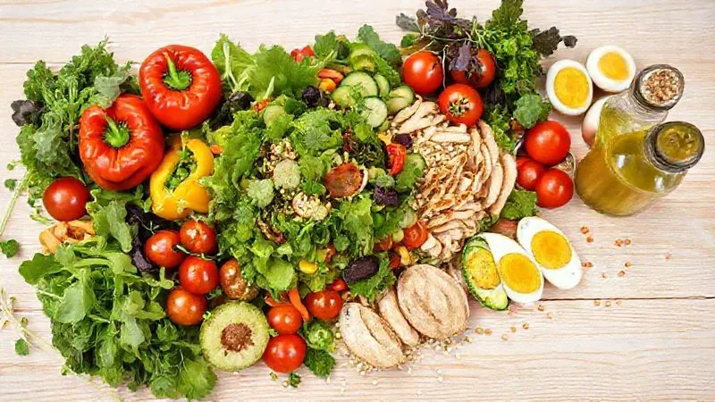 A professional photography shot displaying a vibrant and diverse array of fresh breakfast salad ingredients laid out artfully on a light wooden table. Include various types of leafy greens, colorful bell peppers, cherry tomatoes, cucumbers, boiled eggs, grilled chicken strips, avocado slices, quinoa, a small bowl of mixed nuts and seeds, and a glass bottle of homemade vinaigrette. The composition should be bright, inviting, and emphasize freshness and health. Photorealistic, 8K, cinematic lighting, sharp focus, depth of field, shot on a high-end DSLR.